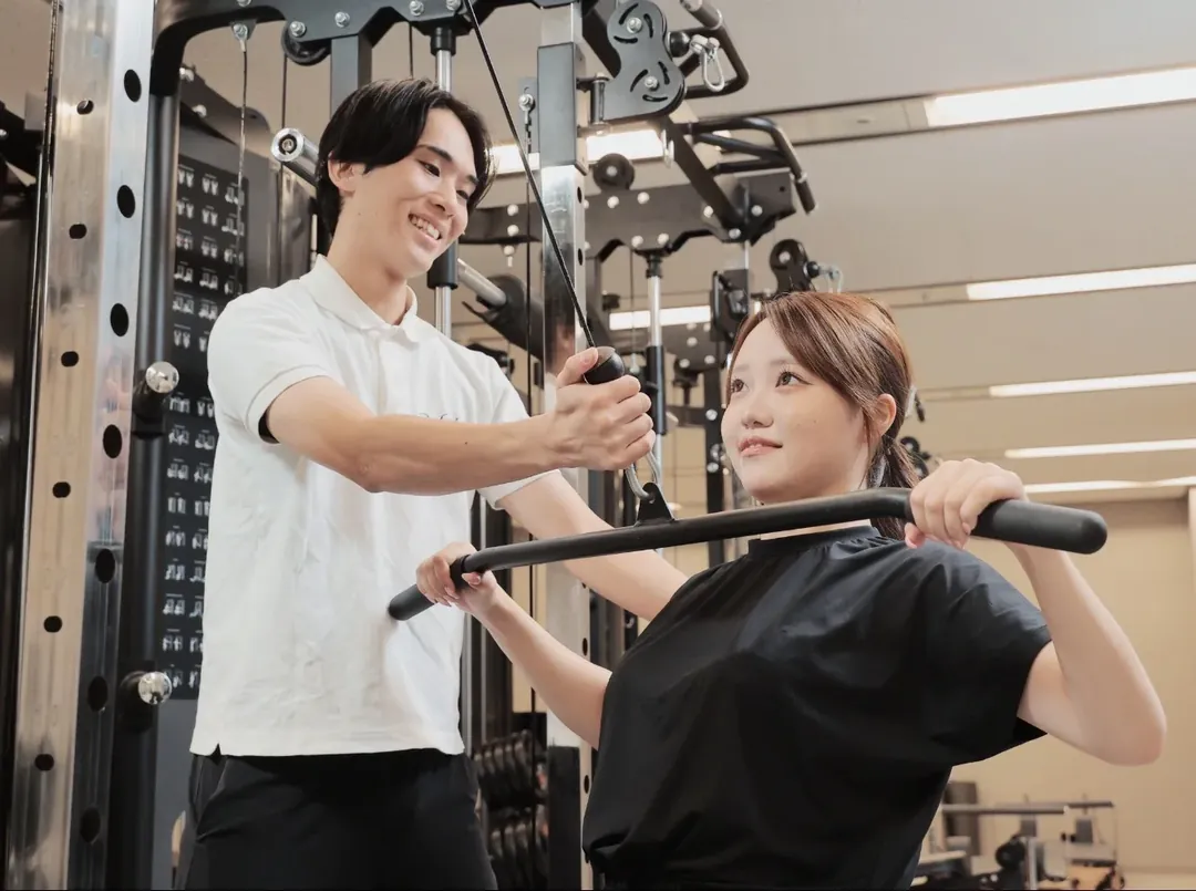 トレーナーの指導でマシントレーニングをする女性