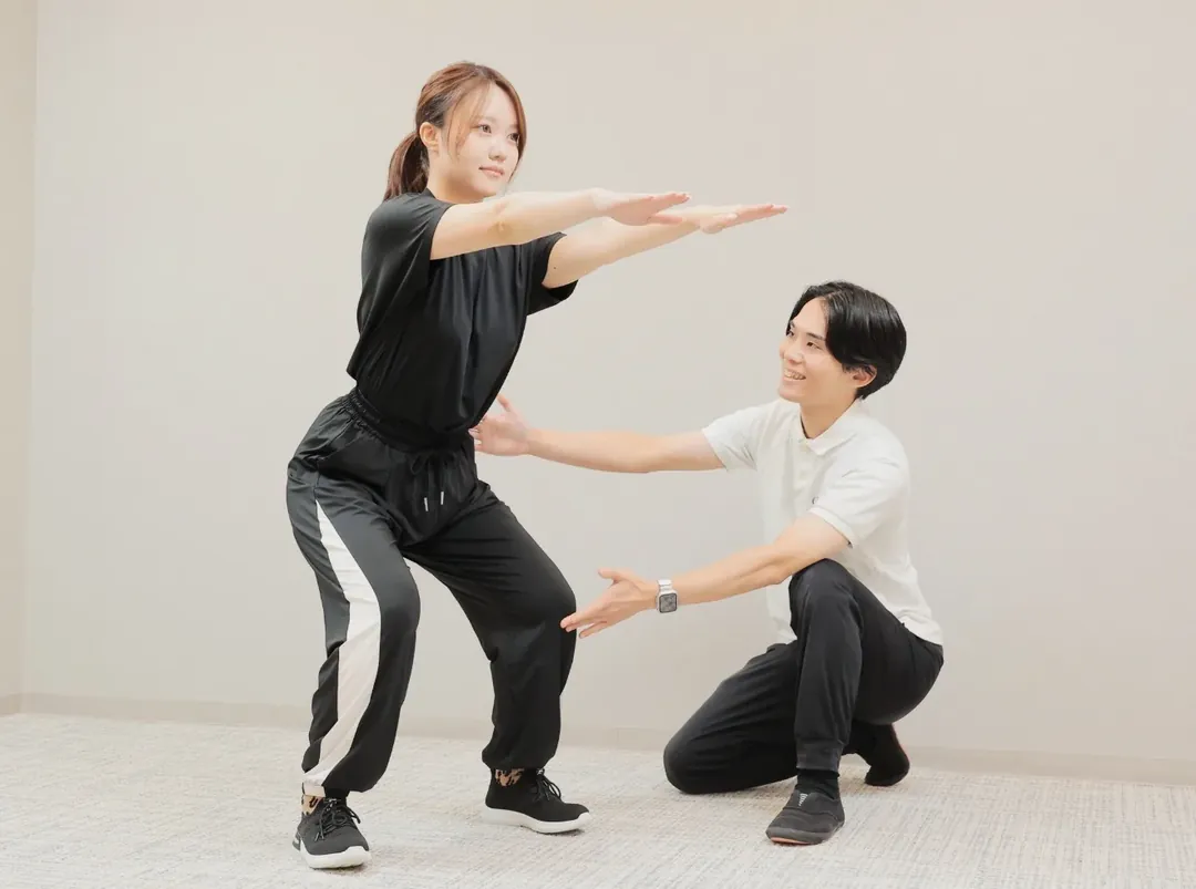 トレーナーの指導でスクワットをする女性